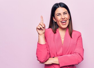 Sticker - Young beautiful business woman wearing elegant jacket standing over pink background smiling with an idea or question pointing finger up with happy face, number one