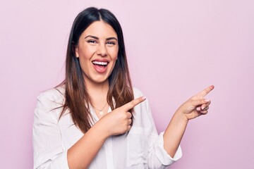 Poster - Young beautiful brunette woman wearing elegant shirt standing over isolated pink background smiling and looking at the camera pointing with two hands and fingers to the side.