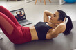 © Studio Romantic - Young woman in activewear doing crunches or sit-ups following instructions of an online trainer