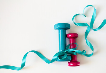 Two turquoise and pink dumbbells with ribbon bow on white background with copy space. Concept Valentines day, male and female, healthy lifestyle, giving gifts, love of sports. Trendy color green tide