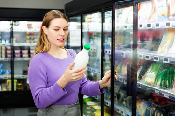 Wall Mural - Young positive cheerful female customer choosing dairy products in supermarket