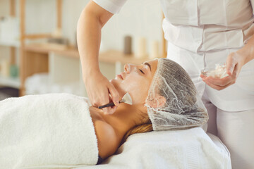 Wall Mural - Beautician covering young womans face with moisturizing mask or cream after skincare procedure