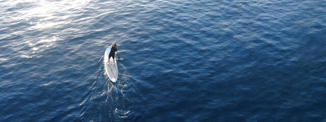 Aerial drone ultra wide photo of fit man practising Stand Up Paddle or SUP in deep blue sea