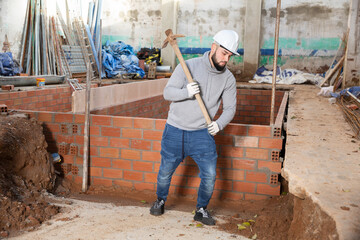 Wall Mural - Young man digging ground with pickaxe, preparing construction pit during house renovations