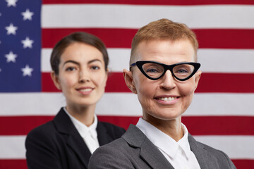 Close up portrait of two confident female politicians looking at camera while standing against USA flag background, copy space