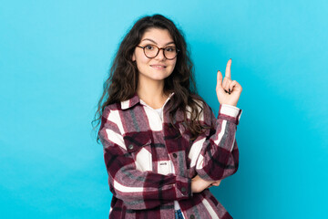 Teenager Russian girl isolated on blue background happy and pointing up