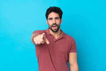 Wall Mural - Young handsome man with beard over isolated blue background surprised and pointing front