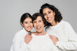 © LIGHTFIELD STUDIOS - Smiling hispanic woman and daughter hugging elderly grandmother isolated on grey, three generations of women