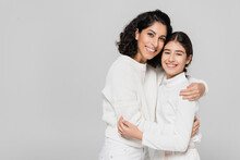 Curly Hispanic Woman Hugging Daughter Isolated On Grey, Two Generations Of Women