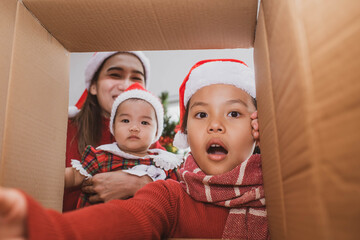 Wall Mural - merry christmas and happy holidays. parent and two little children opening a christmas present. little kid having fun near christmas tree indoors. view from inside of the box. child playing at home