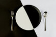 Top view of black and white colors of plate with silver spoon and fork on a black and white background. (text space)