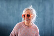 © Halfpoint - Portrait of senior woman with sunglasses standing indoors against dark background, laughing.