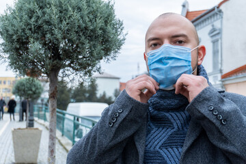 Elegant young businessman poses in city background in face protective mask. Epidemic in the world.