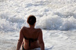 Silhouette on woman in swimsuit sitting in a foaming sea waves, rear view. Beach relax and vacation concept