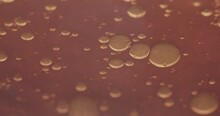 Microscopic Cells And Bubbles Entering Frame From The Left. Waves Moving Over Amber Viscous Liquid. Cinematic Shot Of Scientific Experiment With Oil And Other Chemicals.