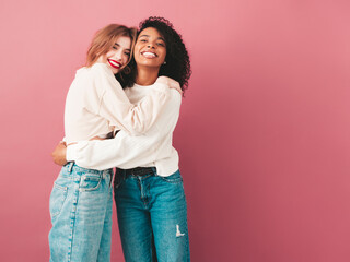 Two young beautiful smiling international hipster female in trendy summer jeans clothes. Sexy carefree women posing near pink wall in studio. Positive models having fun. Concept of friendship