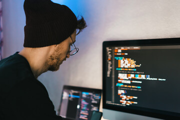 young man mobile developer writes program code on a computer, programmer work in home office.