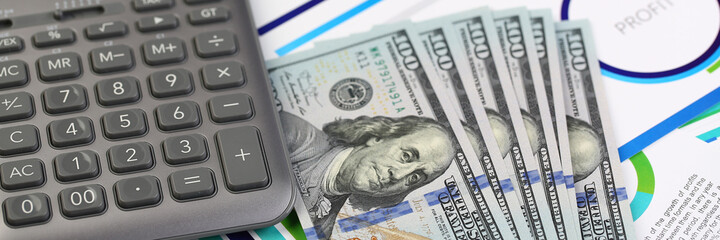 Close up of dollar banknotes, portable electronic device for calculations and silver pen on office desk with documents