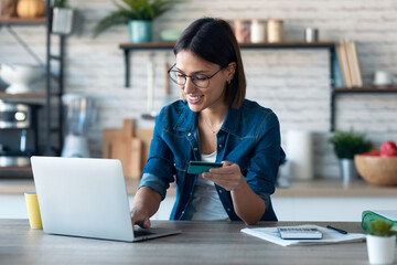 cute young woman holding white credit card for shopping online with computer while sitting in the ki