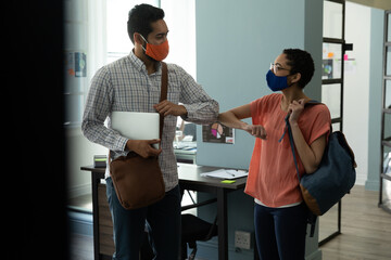 Wall Mural - Mixed race man and woman wearing masks bumping elbows in greeting