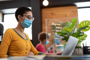 Wall Mural - Mixed race woman wearing face mask working at desk in office