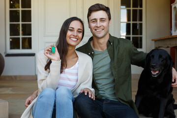 Smiling caucasian couple showing keys sitting outside house with dog