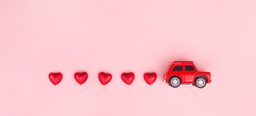 Red retro toy red car with red bow for Valentine's day on pink background with heart. Top view, flat lay, banner