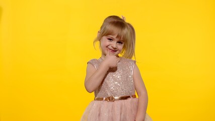 Little smiling blonde child kid girl 5-6 years old in pink dress posing thumb up with hand isolated on yellow background studio. Place for text, logo or product