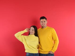 Wall Mural - Happy couple wearing yellow warm sweaters on red background