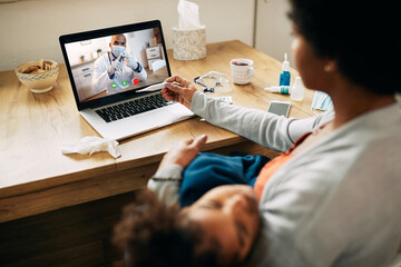 Wall Mural - Close-up of mother having video call with pediatrician while measuring daughter's temperature at home.