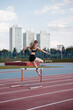 © Alina Hvostikova/Stocksy - Successful sportswoman jumping over hurdle at stadium
