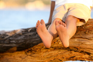 Cute little boy on tree near river, closeup. Child spending time in nature