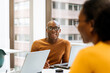 © David Prado/Stocksy - Office employees at conference desk chatting in office