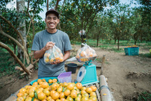 Portrait Of Happy Farmer Selling Orange Fruit With Plastic Bag