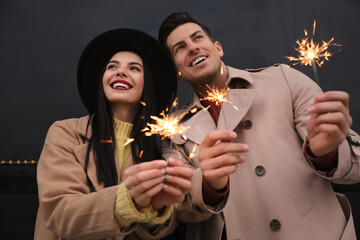 Poster - Couple in warm clothes holding burning sparklers near building