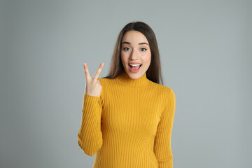 Wall Mural - Woman in yellow turtleneck sweater showing number two with her hand on grey background