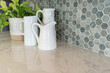 Modern kitchen detail of marble counter with hexagon tile backsplash, white pitchers and potted ivy.