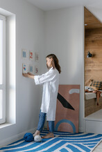 Inspired Woman Hanging Pictures On Wall In Light Room