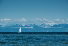 Lone Sailboat Sailing In Blue Waters OfÔøΩLake ConstanceÔøΩwith Alps In Background