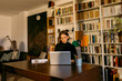© VALENTINA BARRETO STUDIO/Westend61 - Female freelancer working on laptop sitting against bookshelf at home