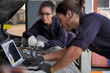 © Surachai - Two young men and women car mechanic I am using a laptop to check and condition the engine.