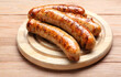Wooden plate with delicious grilled sausages on table