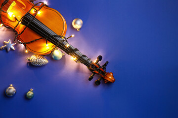 Violin with Christmas lights and decor on color background