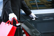 Chauffeur with shopping bags opening door of luxury car