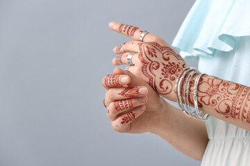 Wall Mural - Beautiful woman with henna tattoo on her hands against grey background, closeup