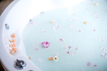 Relaxing bath with milk, flowers and rose petals. Bright room, romantic, relaxing atmosphere.