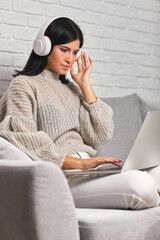 Wall Mural - Beautiful young woman working on laptop while sitting on sofa in living room at home.