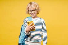 Smiling Male Kid Teen Boy 10s Wearing Striped Sweatshirt Eyeglasses Backpack Using Mobile Cell Phone Typing Sms Message Isolated On Yellow Color Background, Child Studio Portrait. Education Concept.
