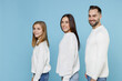 © ViDi Studio - Side view of funny young parents mom dad with child kid daughter teen girl in basic white sweaters looking camera isolated on blue background studio portrait. Family day parenthood childhood concept.
