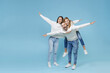 Full length of excited young parents mom dad with child kid daughter teen girl in sweaters giving piggyback ride to joyful, sitting on back isolated on blue background. Family day parenthood concept.